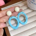 Close-up of blue oval acrylic earrings with cream ball studs on a hand. - Oval Geometric Style (HE32068) / Blue