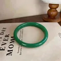 Detailed macro view of a polished green chalcedony bangle placed on a vintage book - Style 2