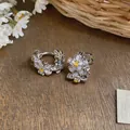 Close-up of elegant zircon flower earrings on rustic wood surface with white floral accents. - Silver-Purple