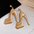 Macro view of gold high heel shoe dangle earrings featuring a shiny metallic finish. - Gold