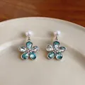 Macro view of floral dangle earrings with teal crystals and white pearl studs - Blue