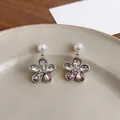 Macro detail of flower earrings with pink crystals and pearls on a beige plate. - Pink