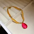 Dettaglio ravvicinato di una collana vintage di perline con un pendente a goccia rosso sfaccettato - Bracciale / Ambra Caffè con Goccia Rossa