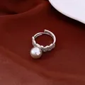 Elegant detail shot of a lace pearl ring with sparkling crystals on dark red fabric. - Grey Pearl / Silver