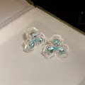 Makroaufnahme eleganter Blumenohrringe mit blauen Zirkoniasteinen und Perlmuttblüten - Silber-Ohrstecker-Stil / Weiß-Blau