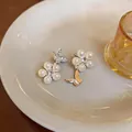Elegant silver-tone butterfly and pearl stud earrings with zircon accents on a white plate - Silver