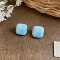 Dettaglio ravvicinato di orecchini a lobo quadrati azzurri con motivo a nuvola - Stile Cubo / Blu