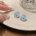 Detail van blauwe emaille bloem oorknopjes met ovale kristallen op een wit bord. - Clip-oorbellen / Goud-Blauw