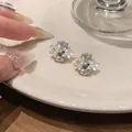 Gedetailleerde weergave van de elegante bloemoorbellen met heldere kristal accenten. - Clip-oorbellen / Goud-Wit