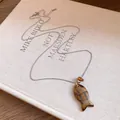 Vue détaillée du collier pendentif poisson en résine avec chaîne argentée sur livre - Marron