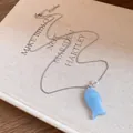 Détail d'un collier avec pendentif poisson en résine bleu clair sur un fond de livre d'art. - Bleu
