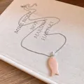 Gros plan détaillé d'un collier avec pendentif poisson en résine sur un livre ancien. - Rose