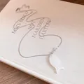 Détail d'un collier pendentif poisson en résine blanche sur une couverture de livre. - Blanc