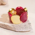 Detailed shot of an acrylic circular patchwork elastic bracelet on a stone base. - Gold-Rose Red
