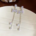 Close-up of elegant silver zircon bow earrings with long shimmering tassels on a dish - Bowknot Style / Silver