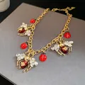 Macro view of vintage gold necklace featuring crystal-winged bees and red ladybug charms. - Necklace / Gold-Red