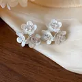 Macro view of elegant silver-tone flower stud earrings with sparkling zircon centers. - Triple Flower Cluster Style / White