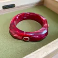 Detailed macro view of a red marble resin bangle featuring elegant ruby-colored rhinestone inlay. - Red