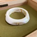Macro view of marbled cream resin bangle with sparkling crystal detail on olive tray - Beige