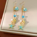 Macro detail of nautical earrings with teal enamel starfish, shells and faux pearls - Gold-Blue Hook Style