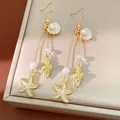 Close-up of golden sea-themed dangling earrings with starfish, shells and pearls. - Ear Hooks - Gold - White