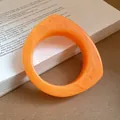 Detail of orange marbled resin bangle with geometric teardrop shape on white book - Orange