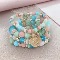 Close-up of Bohemian layered beaded bracelets with an engraved golden heart pendant. - Light Mix