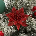 Nahaufnahme einer roten Glitzer-Weihnachtsblume auf schneebedeckten Kiefernnadeln - Rot