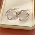Elegantes pendientes de aro entrelazados de color plateado en un joyero de lujo color crema - Plateado
