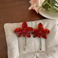 Red enameled flower stud earrings with rhinestone detail on a soft white cushion - Red