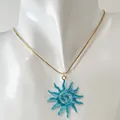 Gros plan d'un pendentif soleil spirale bleu vibrant sur une fine chaîne en or dorée - Collier Soleil Spirale Ajouré (Bleu)