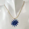 Gros plan détaillé d'un pendentif soleil bleu unique sur une chaîne dorée élégante - Collier Soleil Spirale Ajouré (Bleu Foncé)