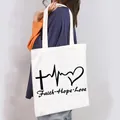 Casual white canvas tote bag with black Faith Hope Love graphic print worn on shoulder - Faith Hope Love Symbol Style (18)