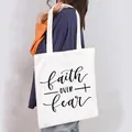 Detailed view of white canvas tote bag with 'Faith Over Fear' print on a model - Faith Over Fear Cross Style (15)
