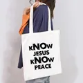 Close-up detail of a white canvas tote bag with black KNOW JESUS KNOW PEACE quote print - Know Jesus Know Peace Style (13)