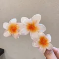 Vue détaillée de trois fleurs de frangipanier sur une pince à cheveux orange translucide - Triple Fleur / Blanc-Orange