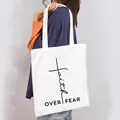 Detail view of a white canvas tote bag with Faith Over Fear print carried by a model - Faith Over Fear Style (1)
