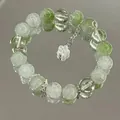 Detail van een groen-witte kralenarmband met een bloemenhanger op een spiegelend vlak - Groen en wit gekraakt model met bloem (S159)