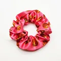 Close-up of a pink satin scrunchie with orange basketball prints - Pink Base Basketball