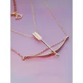Rose gold bow and arrow necklace pendant with heart detail on a pink gradient background. - Rose Gold