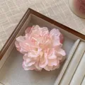 Detailansicht einer eleganten rosa-weißen Pfingstrosen-Haarklammer in einer Holzschale. - Rosa & Weiß