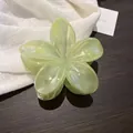 Détail d'une pince à cheveux en résine vert clair en forme de frangipanier sur bois sombre - Vert