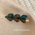 Elegant triple heart hair clip featuring teal and amber glass texture on a beige stone background - Dark Teal