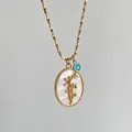 Détail d'un collier ovale vintage avec branche de fleur dorée et breloque en pierre bleue - Décembre - Poinsettia