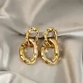 Gros plan de boucles d'oreilles créoles dorées irrégulières sur fond de soie élégant - Entrelacé Ondulé Or (E5452-1)