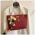 Close-up detail of a burgundy quilted shoulder bag with silk scarf and gold chain - Red