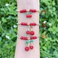 Primo piano di tre braccialetti con ciliegie e perline rosse e dorate su un polso. - Set da 3 Pezzi Ciliegia Zirconia (E1)