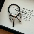 Close-up of a silver metallic bow hair tie displayed on a textured fabric background - Silver Bowknot