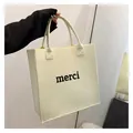 Close-up detail of a minimalist cream felt tote bag with 'merci' text print held in hand - Milky White