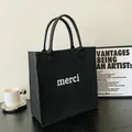 Close-up of a minimalist black felt tote bag with white merci text on a modern desk. - Black / 23x23x13cm